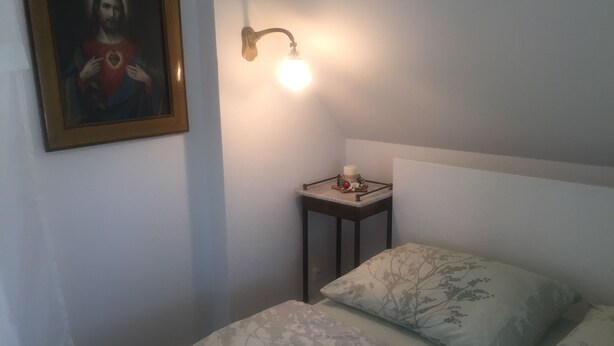 A bedroom with a bed, a nightstand with a lamp, a framed picture on the wall, and a small table with decorative items. - Charming 2-bedroom cottage in Pavlov with WiFi access (Pavlov)