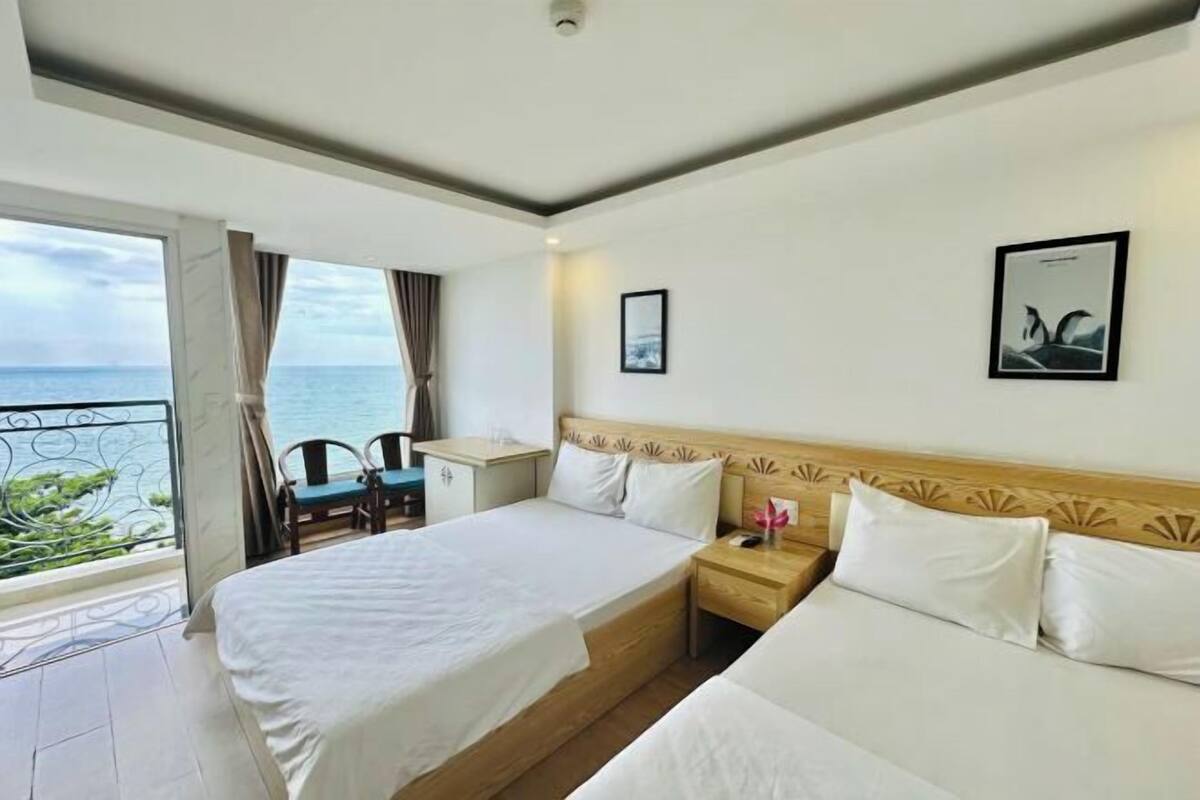 A hotel room with a balcony, a bed, a bedside table, a chair, and a view of the sea.