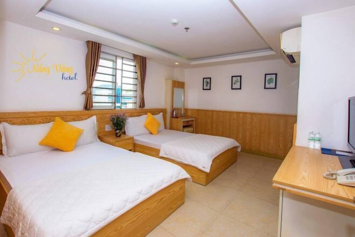 A hotel room with two beds, a desk, a television, and a window with curtains.
