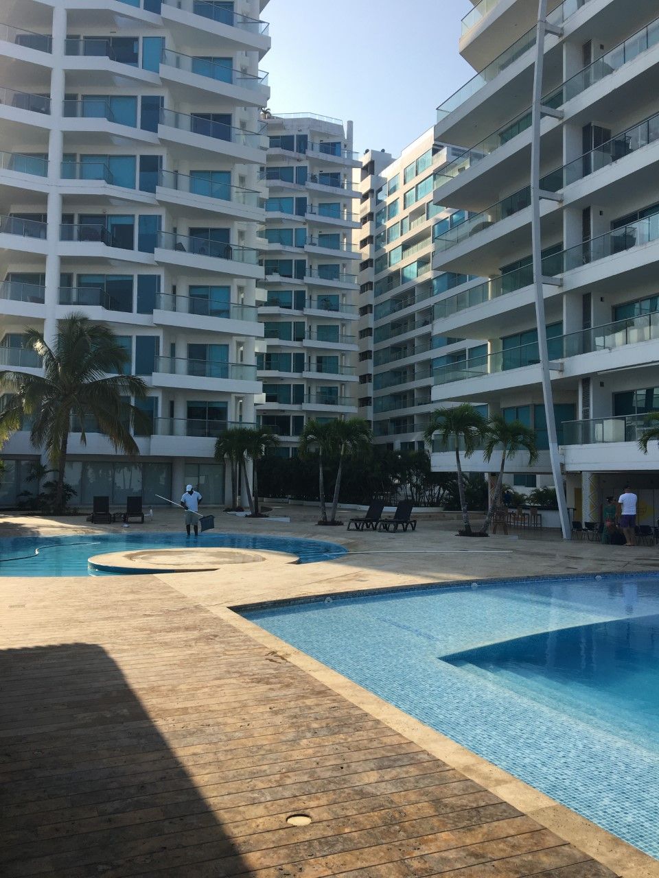 A modern hotel with multiple balconies, a swimming pool, and palm trees.