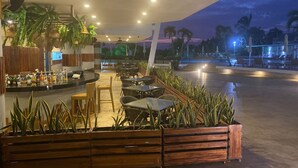 An outdoor seating area with tables and chairs, surrounded by planters and a bar counter with bottles.