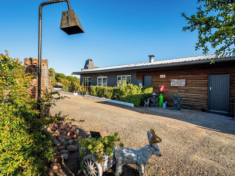 A rustic cabin with a gravel driveway, surrounded by greenery and decorative statues.