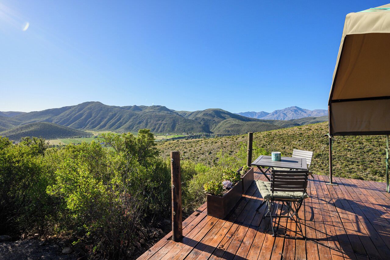 Une terrasse en bois avec une table et des chaises, offrant une vue sur un paysage montagneux.