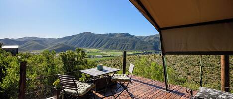 An outdoor deck with a table and chairs, overlooking a mountainous landscape.