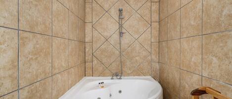 A bathroom with a white bathtub, tiled walls, and a wooden chair.