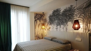 Una camera da letto con copriletto a quadri, un comodino con lampada e un affresco raffigurante alberi.