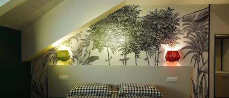 Une chambre avec une couvre-lit à carreaux, deux lampes de chevet et une fresque murale représentant des arbres.