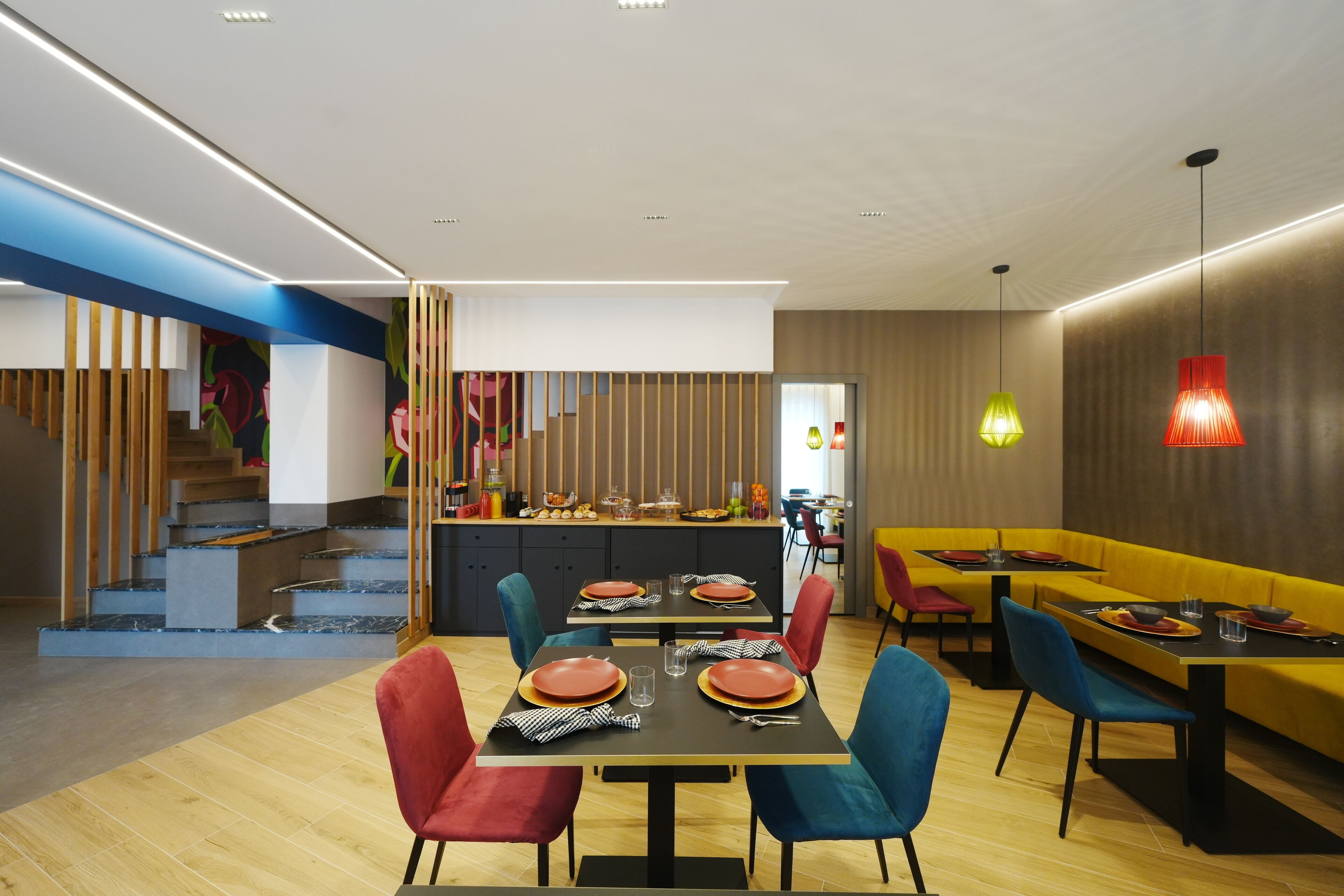 Un espace repas moderne avec un plancher en bois, une table centrale entourée de chaises et un coin salon jaune en arrière-plan.
