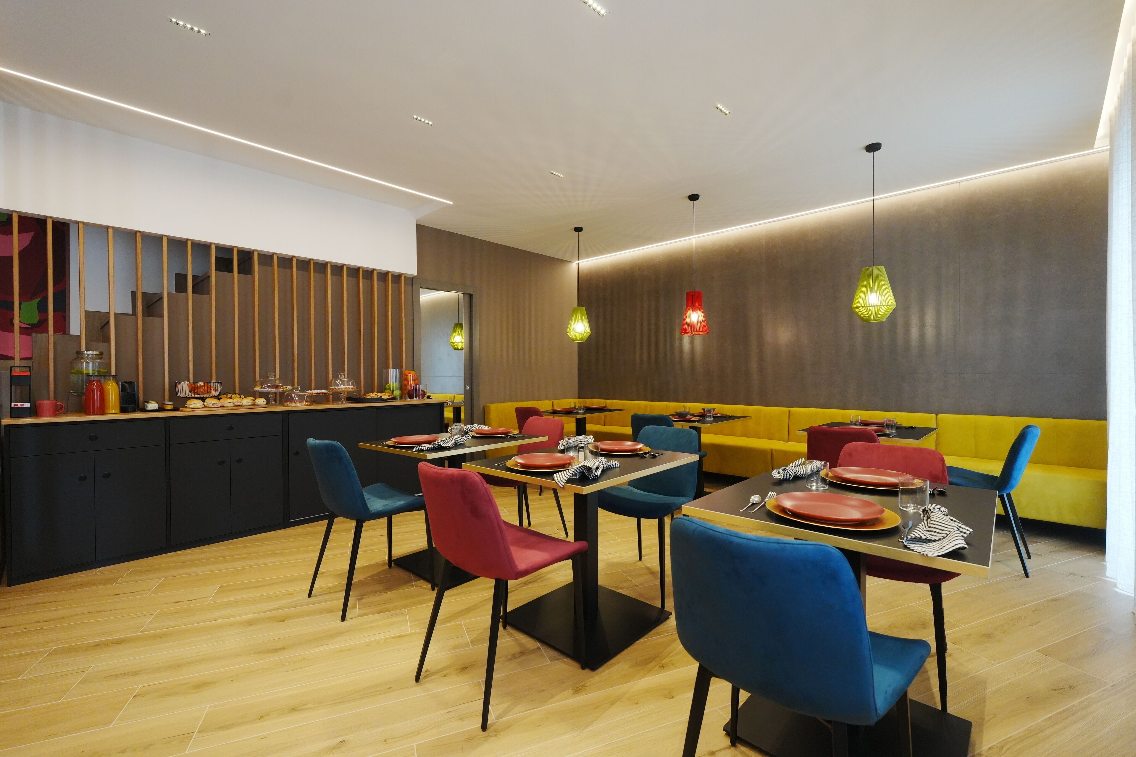 Ein modernes Restaurant mit Holzböden, blauen und roten Stühlen sowie gelben Sitzbänken.