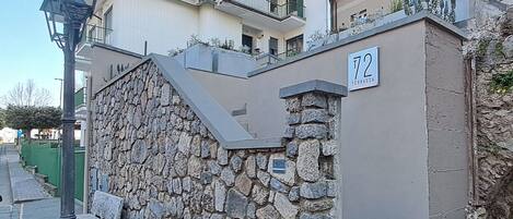 Un mur de pierre avec un escalier menant à un bâtiment. Une plaque portant le numéro 72 est visible sur le bâtiment.