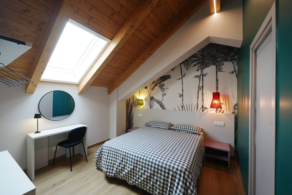 A bedroom with a skylight, a desk, a bed, and a wall mural.