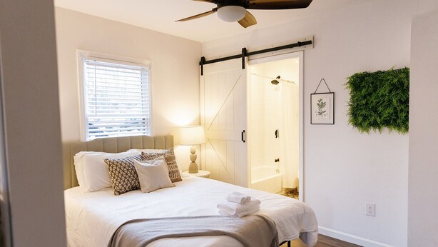 A bedroom with a bed, bedside table, lamp, and a ceiling fan.