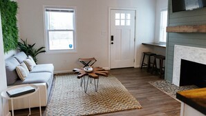 A living room with a grey sofa, a unique wooden coffee table, a fireplace, and a green wall decoration.