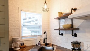 A kitchen with a window, a coffee maker, a sink, and shelves with jars.