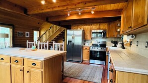 Una cocina amplia con armarios de madera, una isla grande, electrodomésticos de acero inoxidable y una escalera de madera que sube a un nivel superior.