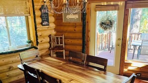 Interior de madera con una gran mesa de comedor, sillas, una araña y una puerta que da al exterior.