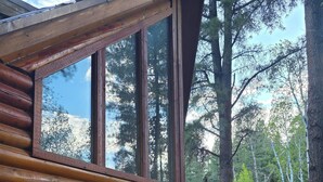 Una cabaña de troncos con amplios ventanales, una terraza y mobiliario exterior.
