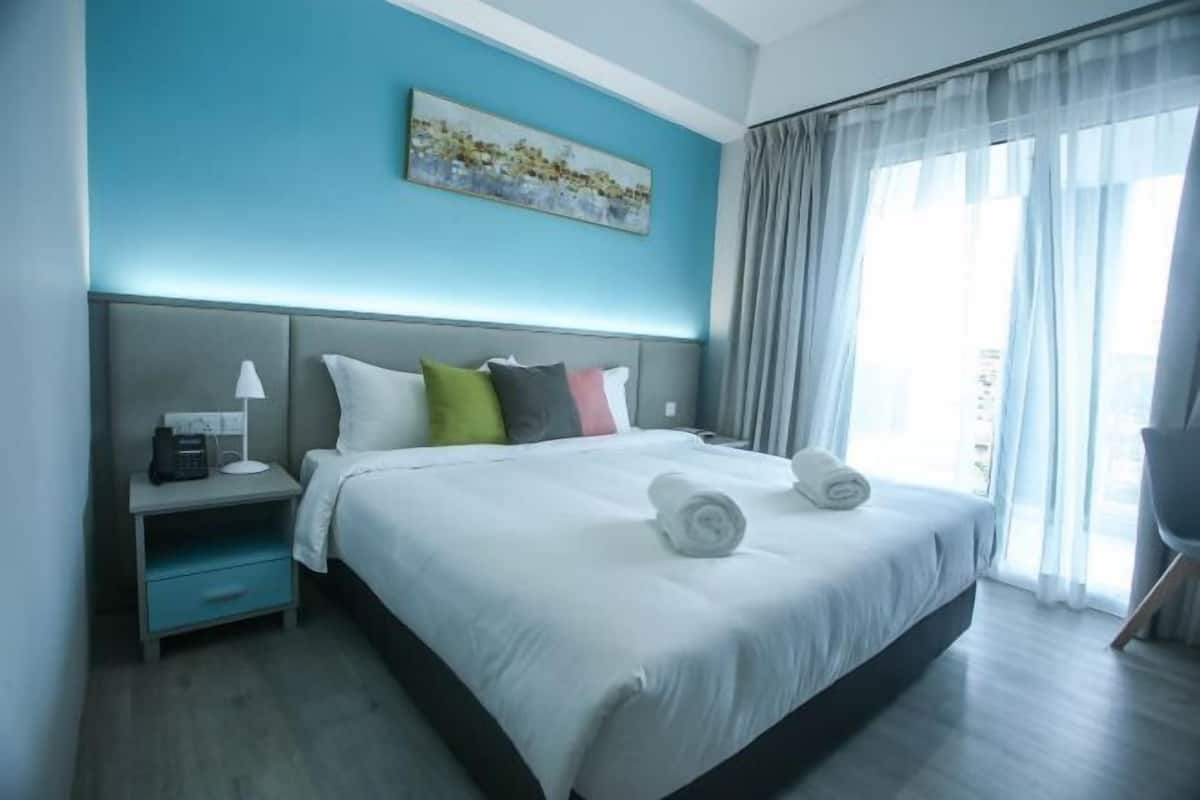 A hotel room with a bed, a nightstand, a lamp, a painting on the wall, and a window with curtains.