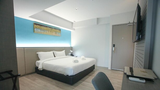 Una habitación de hotel moderna con una cama, un escritorio, una silla, un cuadro en la pared y una puerta.