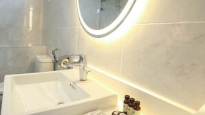 Un baño moderno con un espejo ovalado grande, un lavabo y una ducha.