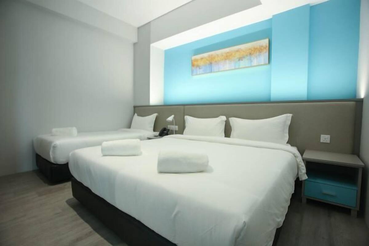 A hotel room with two beds, a nightstand, a wall-mounted painting, and a blue accent wall.