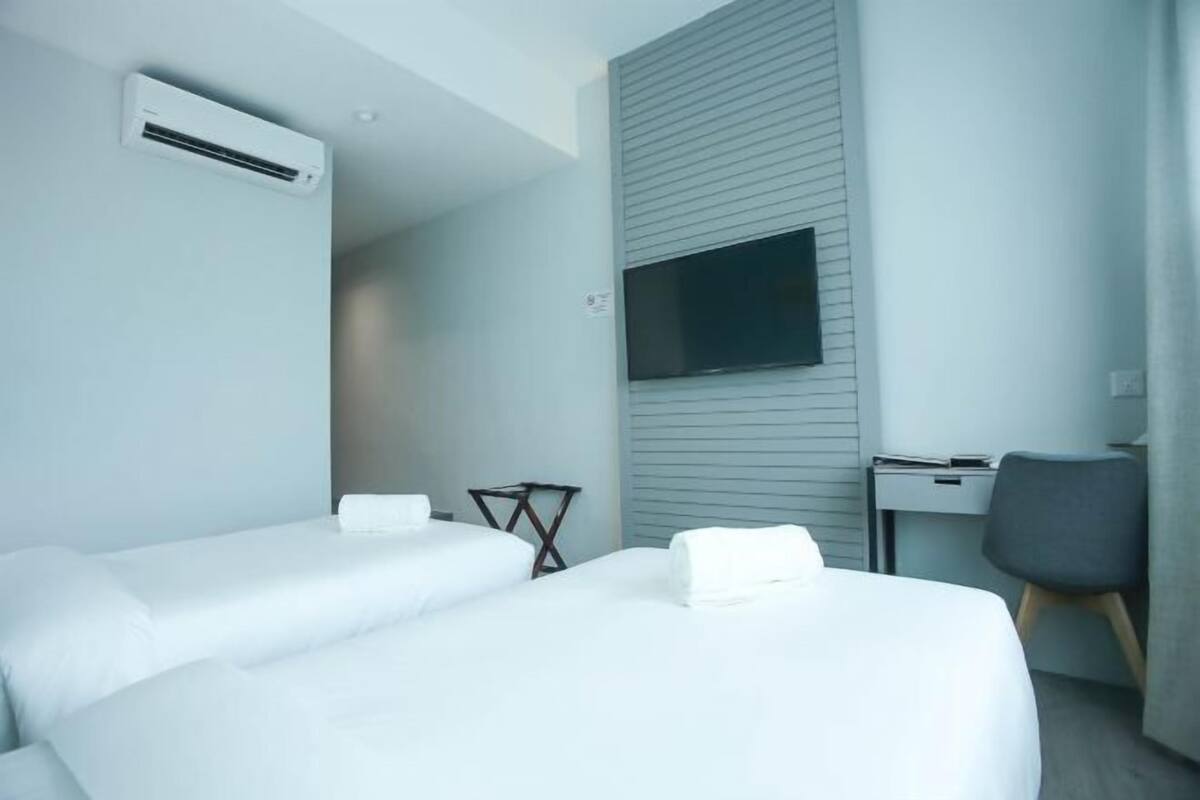 A hotel room with two beds, a desk, a chair, a TV, and an air conditioning unit.
