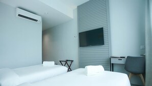 Habitación de hotel con dos camas, un escritorio, una silla, un televisor de pantalla plana montado en la pared y un equipo de aire acondicionado.