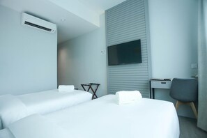Habitación de hotel con dos camas, un escritorio, una silla, un televisor de pantalla plana montado en la pared y un equipo de aire acondicionado.