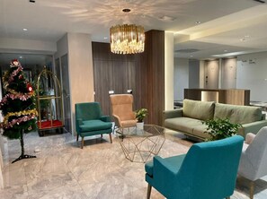 A modern living room with a glass coffee table, teal armchairs, a beige sofa, and a decorative Christmas tree.