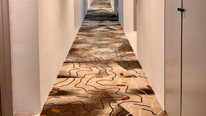 Un pasillo largo y estrecho con alfombra estampada y paredes blancas.
