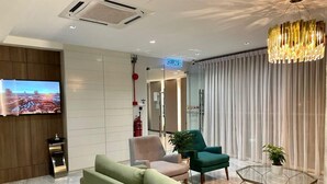 Un moderno vestíbulo de hotel con un sofá, sillas, un televisor, una mesa de centro de vidrio y una araña.