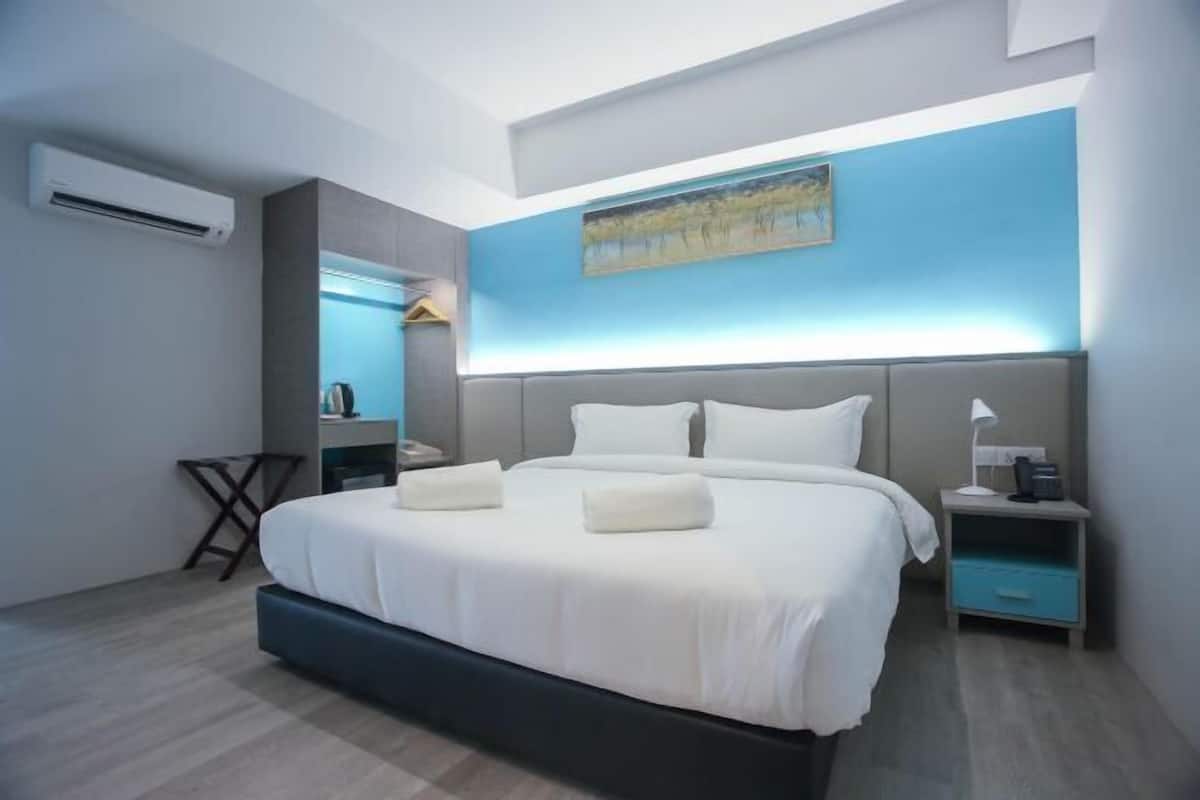 A modern hotel room with a large bed, bedside tables, an air conditioning unit, and a painting on the wall.