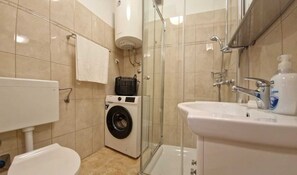 Un baño compacto con lavadora, inodoro, lavamanos y cabina de ducha.