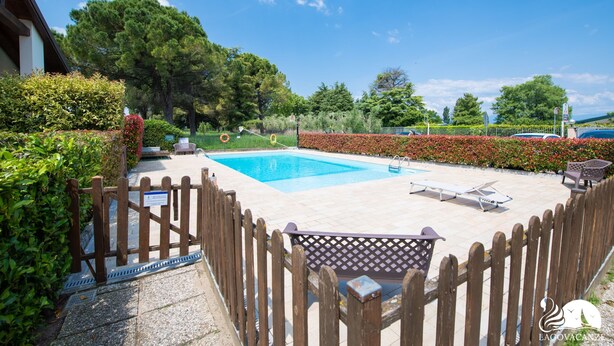 Una piscina con valla de madera, sillas de descanso y solárium empedrado.