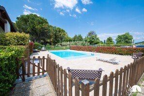 A swimming pool with a wooden fence, lounge chairs, and a paved deck.