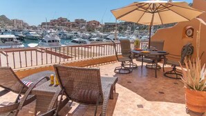 Eine Terrasse mit Korbstühlen und einem Tisch, mit Blick auf einen Yachthafen und Boote.