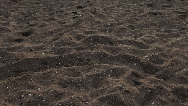 A beach with footprints and a flag, under a cloudy sky with the sun setting.
