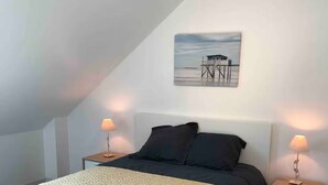 A bedroom with a bed, two bedside tables, a nightstand, a wall-mounted picture, and a sloped ceiling.