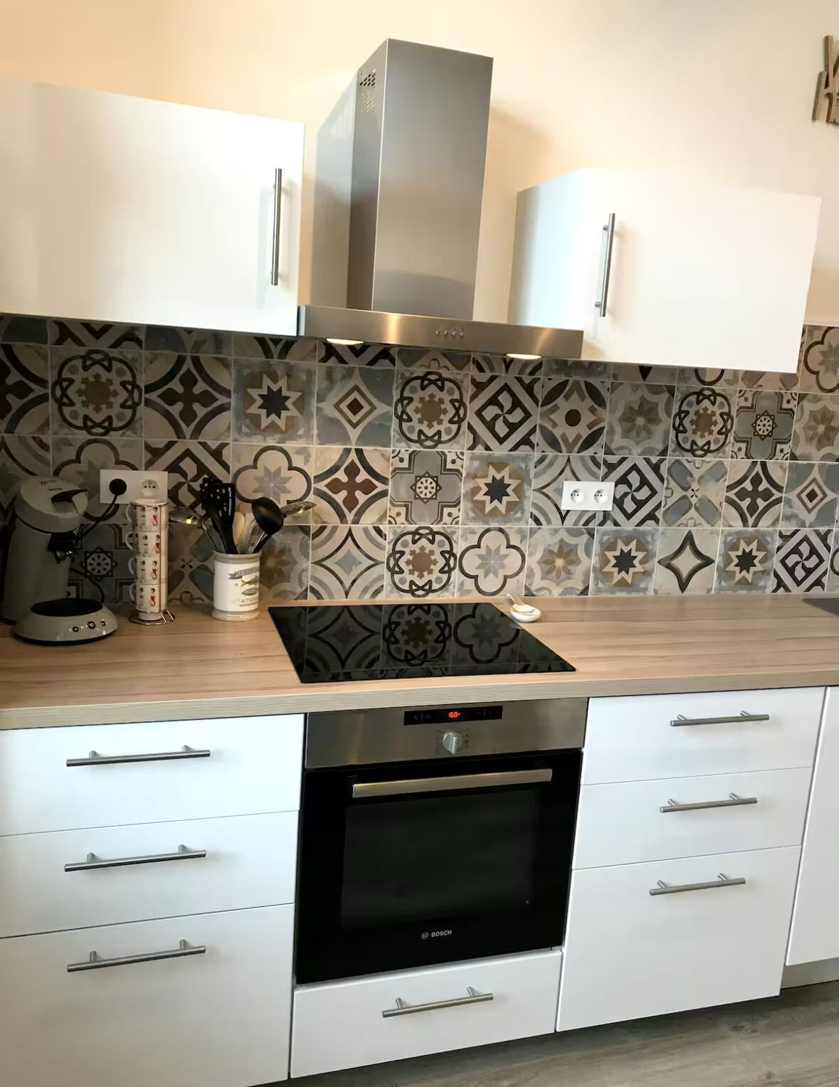 Une cuisine moderne avec des armoires blanches, un four Bosch et des carreaux décoratifs sur le mur derrière l’évier.