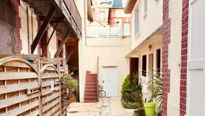 A narrow stone-paved alleyway between buildings with a wooden gate on the left and a white door on the right.