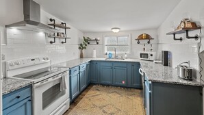 A modern kitchen with white and blue cabinetry, a built-in oven, a stainless steel range hood, and a granite countertop.
