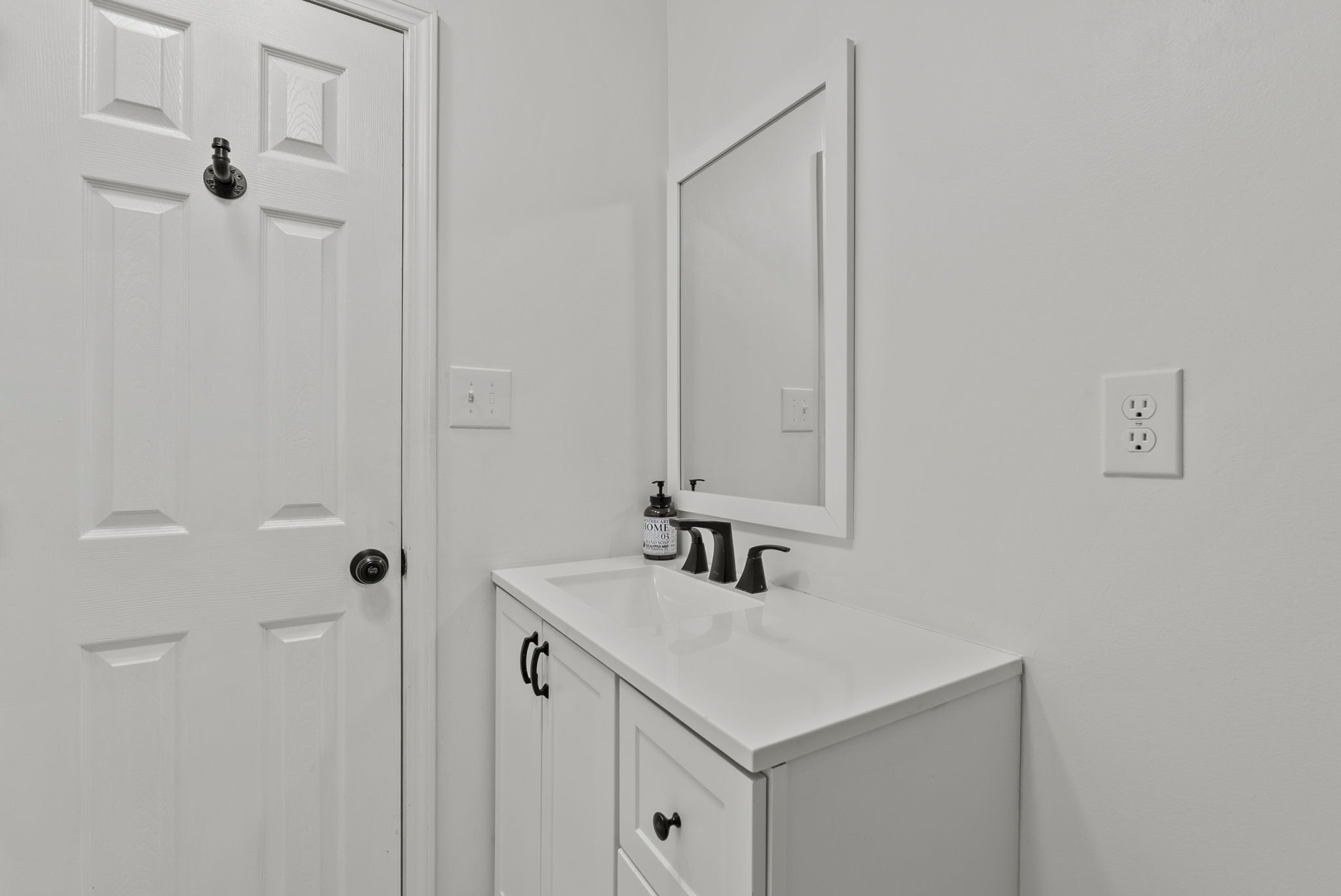A white bathroom with a door, a mirror, a sink, and a cabinet.