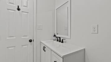 A white bathroom with a door, a mirror, a sink, and a cabinet.