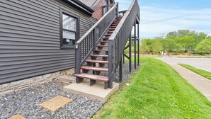 A residential building with a gray exterior, a wooden staircase leading to a porch, and a well-maintained lawn.
