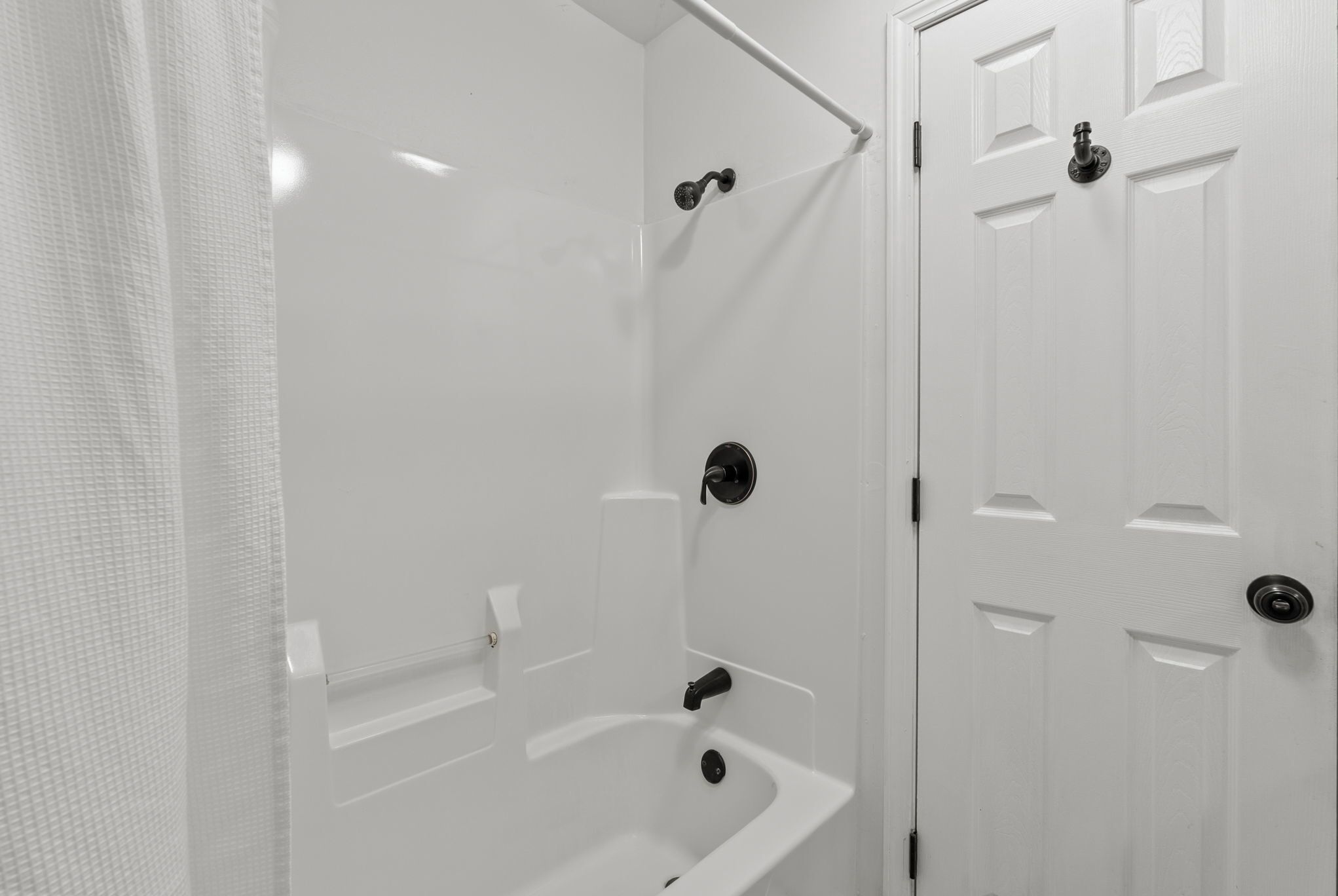 A bathroom with a bathtub, a shower, and a door with a handle.