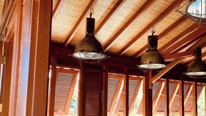 A wooden interior with a sloped ceiling, built-in benches, and hanging pendant lights. - Ecolodge Anacardier- Bungalow Deluxe 1 (Saint-Francois)