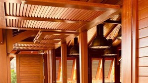 A covered outdoor seating area with wooden benches and tables, a wooden floor, and a view of the surrounding landscape. - Ecolodge Anacardier- Bungalow Deluxe 1 (Saint-Francois)