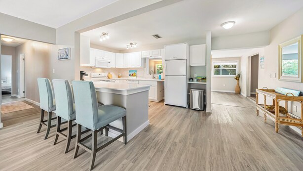 A modern kitchen with white cabinets, a central island, and a dining area with four chairs.