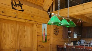 En matplats med träinredning, ett långt bord och stolar, en hängande grön lampa och ett träpanelat tak med en dekorativ väggdekoration.