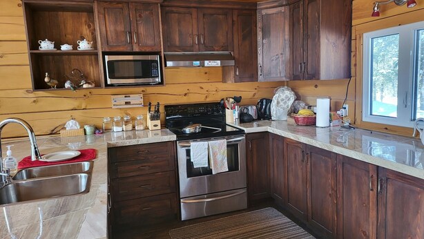 A kitchen with wooden cabinets, a stainless steel stove, a microwave, and a window with a view.